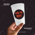 White cup with 'You're Next' Halloween design held by a hand against a dark background
