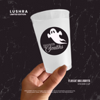 White cup with Halloween-themed sticker held by a hand on a dark background, featuring Lushra branding.