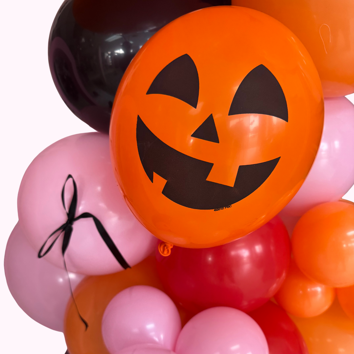 Halloween-themed balloons with a jack-o'-lantern design and pink balloons with black ribbons.