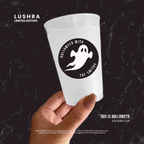 White cup with Halloween-themed sticker held by a hand against a black background, featuring Lushra branding.